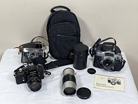 Group view of three cameras, telephoto lens, cases and bag