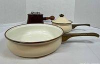 Three enamel pans: brown Dansk saucepan with lid; ivory La Cuisine frying pan; ivory La Cuisine saucepan with lid