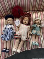 Three dolls lying on striped surface: blue check, white with red trim, teal romper