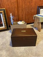 A single dark brown wooden box positioned on the floor, showing top and front side (lid) with metal plate and keyhole, minor surface scratches visible.