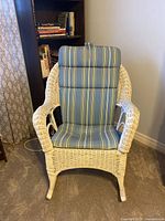 Frontal view of the white wicker armchair with blue and green striped seat and back cushions shown in a room.