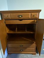 Interior view of armoire with double doors open, revealing divided shelving and exposed top drawer beneath cabinet shelf.