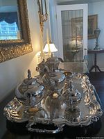 Silver-plated tea set on ornate tray displayed on a table with mirror reflection