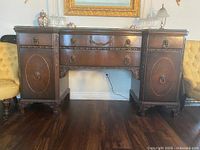 Front view of vintage dark brown wood buffet showing lion head drawer pulls on drawers and side doors with carved details.