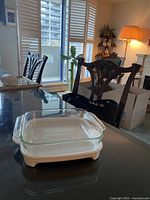 Two white individual baking dishes including one rectangular and one square with glass insert, shown on glass table.