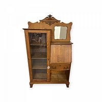 Front view of entire secretary desk bookcase showing carved crest, glass door, mirror, drop-front desk and drawer.