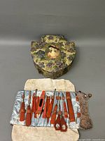Photo of closed Victorian dresser box with floral pattern and woman's portrait on lid, displayed with the open manicure set pouch showing Bakelite handled tools inside.