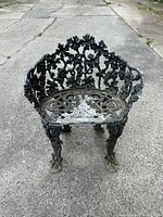Front view of rustic metal garden seat showing decorative backrest with floral and vine patterns and claw-foot legs.