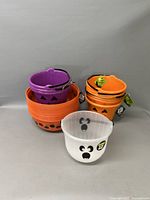 Stacked Halloween-themed plastic buckets in orange and purple, white ghost bowl in front