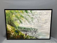 Full view of the framed landscape oil painting showing a riverbank with a person fishing beneath a large leafy tree.