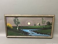 Framed oil painting of a moonlit landscape showing a full moon, flowing stream, trees, and a small structure in the distance