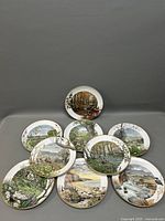 Nine Peter Barnett cabinet plates arranged on a grey background, showing full front views with detailed naturalistic scenery artwork on each plate.