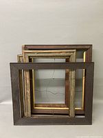 Four picture frames stacked with a black rectangular frame in front, showing wear and different materials and styles.