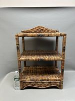 Front view of the rattan shelf showing all three tiers and backsplash with a water bottle for scale