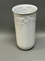 Front view of the white ceramic vase showing embossed floral designs in relief, cylindrical shape.