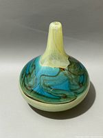 Art glass vase with a swirl design of blues, turquoise, brown, and cream colors. Narrow neck and rounded body shape.