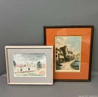 Two framed artworks against a gray background, one a watercolor landscape and one a colored etching of a village.