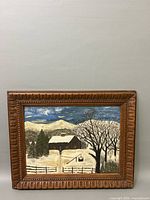 Full view of framed oil painting showing winter scene with cabin, snow, trees and mountains.