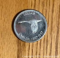 Reverse side of the 1967 Canadian 1 dollar coin showing a flying Canada goose and commemorative dates 1867-1967.