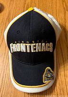 Front view showing embroidered Kingston Frontenacs text and team patch on brim, navy and white color with yellow piping.