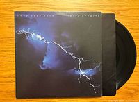 Front cover of Dire Straits 'Love Over Gold' vinyl record album with clear lightning storm artwork and visible black vinyl on wooden surface.