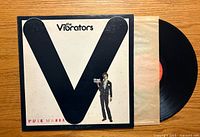 Front cover of The Vibrators Pure Mania vinyl record showing the large black "V" design and a man holding a vinyl record.