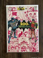 Photo of Batman #200 comic book showing front cover featuring Batman and Robin in color over a background of monochrome comic panels in red and white, with '200th Smash Issue' badge in center.