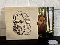 Wooden box with engraved portrait of Eden Ahbez on the lid next to album cover featuring photo of Eden Ahbez