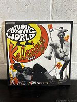 Front cover of the vinyl record showing the Kelenkye Band 'Moving World' album artwork with two band members and stylized text and graphics.