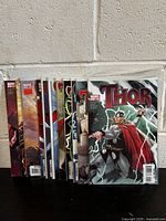 Photo shows a lot of 12 Thor comic books including standard and variant covers, displayed upright against a wall.