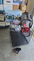 Black metal dog kennel with collapsible gray pet carrier on top, including Pet to Go Travel Bag accessory set box and various pet items on kennel.