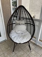 Front view of egg-shaped wicker chair with seat cushion and lumbar pillow