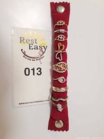 Nine fashion jewellery rings displayed vertically on padded red fabric strip for clear view of each ring's design and size.