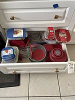 Drawer with glass and plastic food storage containers with matched lids, red, blue, and green lids, Pyrex and Anchor visible