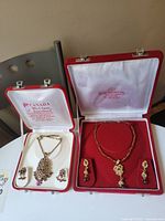 Two Indian jewelry sets in boxes: left set with gold-tone and purple stone necklace and earrings; right set with gold-tone, red beaded necklace and matching earrings.