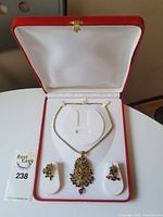 Full view of necklace and earring set inside red and white jewelry box, showing arrangement of items and packaging.