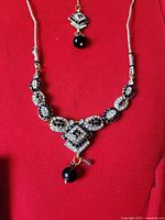 Front view of the necklace showing detailed craftsmanship, clear stones, and black bead pendants on a red background.