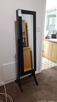 Front view of tall black wooden jewelry cabinet with full-length mirror and lock.