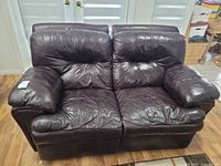 Front view of the two-seat brown leather love seat showing padded armrests and cushioned seats