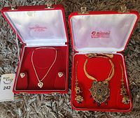 Both jewelry sets shown side by side inside their boxes on a textured surface.