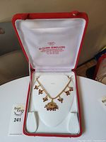 Red jewelry box with white interior lining, holding a gold tone necklace with gemstone accents.