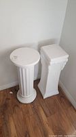 Pair of decorative plaster pillars - one round and one square placed on wood floor next to wall