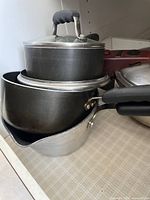 Stack of three black and aluminum pots and saucepans with one glass lid