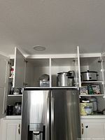 Kitchen cabinets open showing large stainless steel pots and kitchen appliances stored inside, metal rice cooker visible.