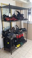 Black metal shelving rack with wire mesh shelves filled with various bags (bags not included)