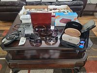 Full overview of sunglasses, cases, and storage box laid on wooden table.