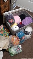 Plastic bin with multiple skeins of yarn in purple, pink, black, white, yellow, multicolor, and turquoise colors, in and around the bin with some bagged yarn balls.