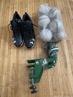Pair of black Under Armour size 10 baseball cleats, bag of 10 white softballs, green clamp ping pong net on wooden floor