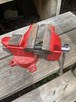 Side view of the red 3 1/2 inch bench vise on a wooden surface showing jaws, handle, and mounting holes.