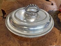 Oval silver plated serving dish with a domed lid and decorative beaded edge, showing entire closed item.